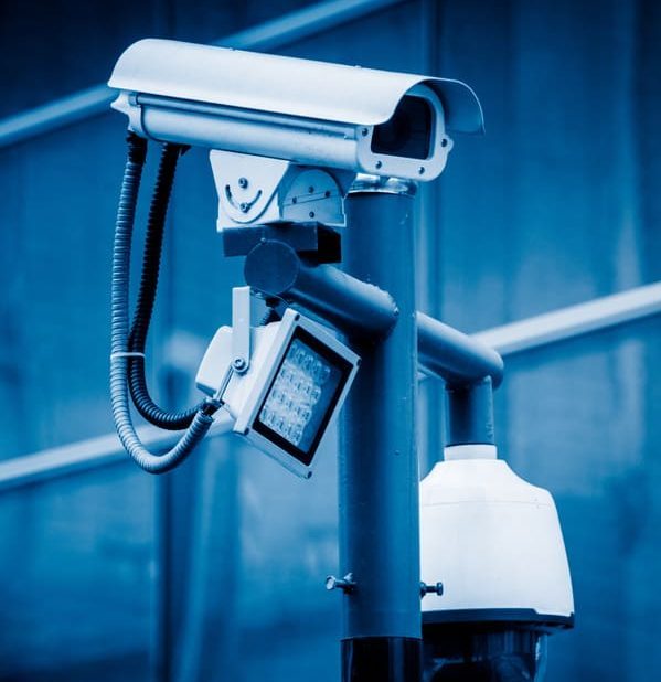 A CCTV security camera mounted against a building, depicted in blue tone.